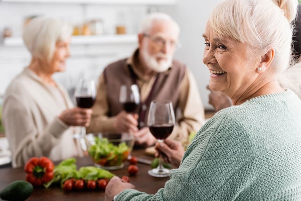 happy-senior-woman-holding-glass-red-wine-retired-friends-blurred-3